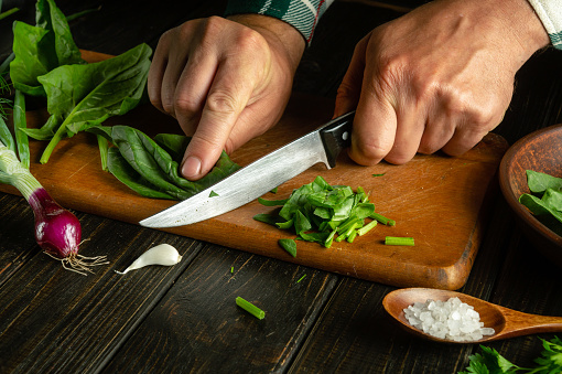 Chef hands cut spinach with a knife on a kitchen cutting board. Preparing vegetarian food in the kitchen. Vegetable diet concept.