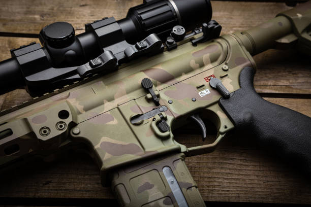 istock A modern carbine with an optical sight and a silencer. Weapons in camouflage coloring. Old wooden background. 1776691450
