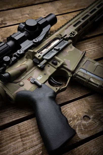 istock A modern carbine with an optical sight and a silencer. Weapons in camouflage coloring. Old wooden background. 1776691452