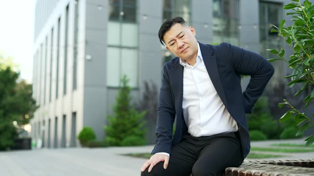 Tired overworked asian businessman in formal suit suffering from back pain