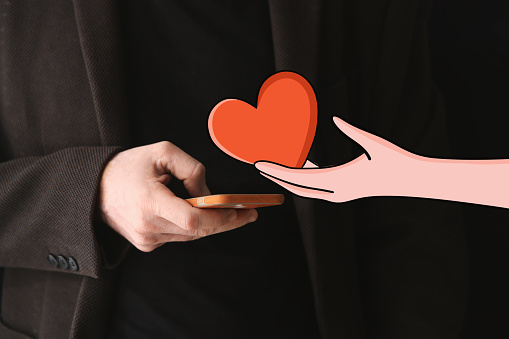 Man holds a mobile phone in his hand and the hand holding a heart extends the heart