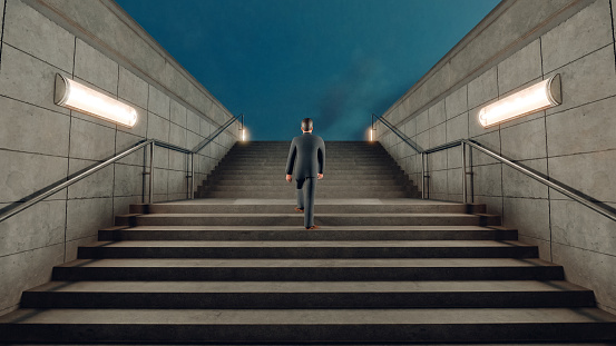 Man in suit walks up the stairs at a subway station into the light. Concept of walking the ladder of succes.