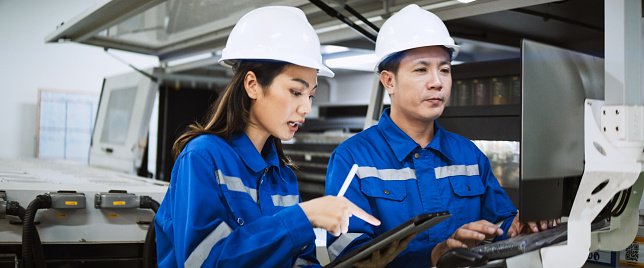 Young adult Asian man, woman engineer worker work together in factory warehouse, discuss talk, use computer machine. Teamwork communication, logistic industry business, people at industrial work