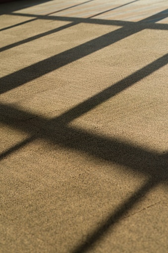 An empty building with a door featuring cast iron bars, with sun-cast shadows creating an interesting visual pattern