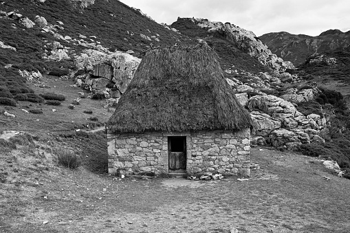 A traditional thatched roof stone hut nestled in a picturesque hillside landscape with a stunning mountainous backdrop