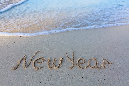 Word new year written on the sand of the beach. Beach and wave background.