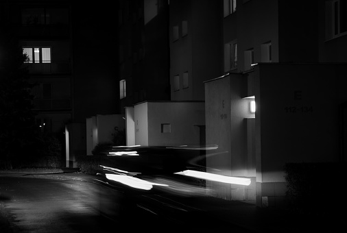 A young adult is strolling down a deserted urban street at night, illuminated by street lamps