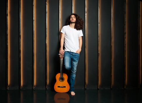 Music Star. Full Length Shot Of Young Latin Musician Man Posing Holding Acoustic Guitar, Looking At Camera Standing Near Black Wall In Studio. Express Your Talent Concept