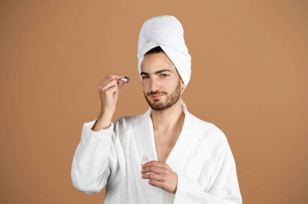 istock Man in White Bathrobe Applying Facial Serum On Beige Background 1776805641