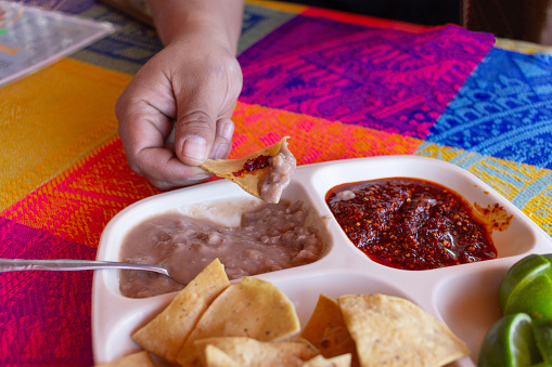hand holding corn tortilla chips with beans and spicy macha sauce