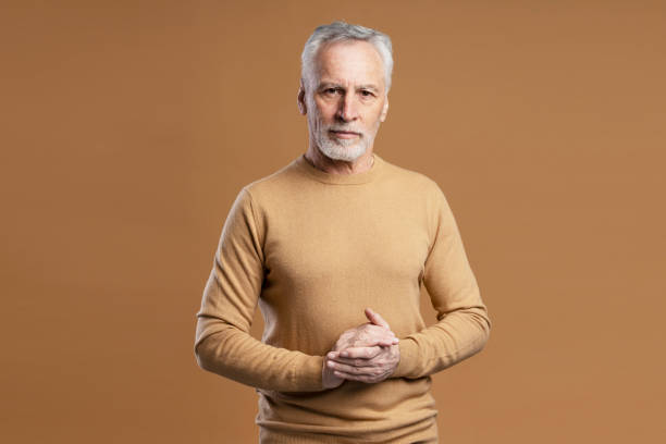 atrakcyjny starszy mężczyzna stojący na białym tle na brązowym tle. siwowłosy 60-letni mężczyzna - 60 65 years zdjęcia i obrazy z banku zdjęć