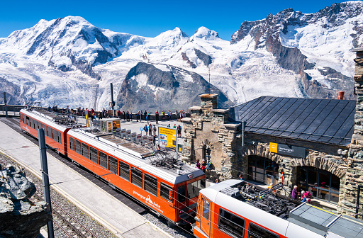 Kleine Scheidegg, Bernese Oberland, Switzerland - August 1 2019 : Famous red train to Jungfraujoch with snow capped Eiger north face, Monch and Jungfrau in the background