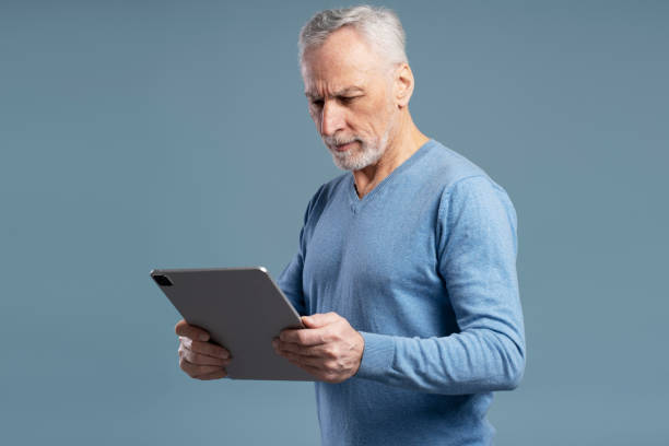 istock Serious senior man using tablet isolated on blue background. Mature businessman checking email 1776860574
