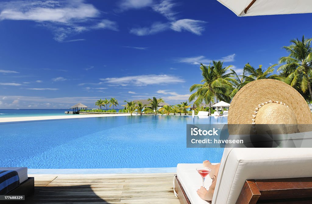 Woman at poolside with cosmopolitan cocktail Woman in hat relaxing at the poolside with cosmopolitan cocktail Maldives Stock Photo