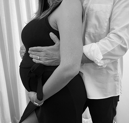 Brazilian couple in late pregnancy arms forming loving embrace over the baby bump in close up