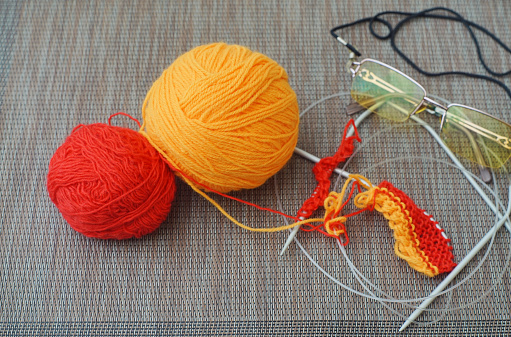 High angle view of balls of knitting thread, knitting needles and reading glasses.