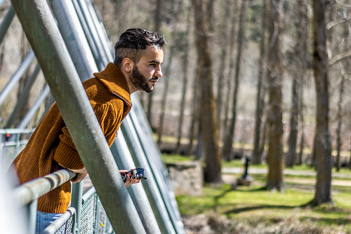 thoughtful young man leaning on a bridge looking at nature