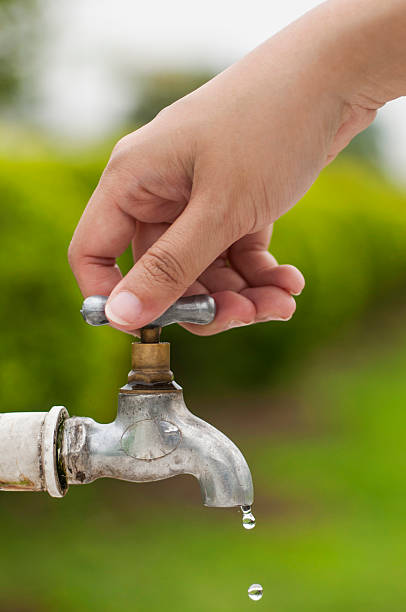 Hand turning off dripping outdoor water faucet stock photo