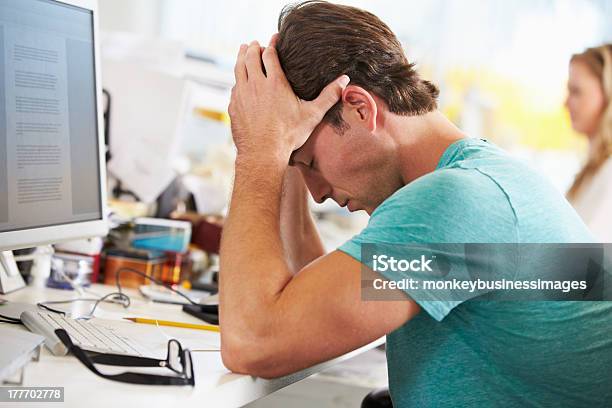 Stressed Man Working At Desk In Busy Creative Office Stock Photo - Download Image Now