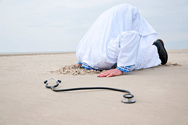 masculino médico stucks a cabeça na areia - overstrained imagens e fotografias de stock