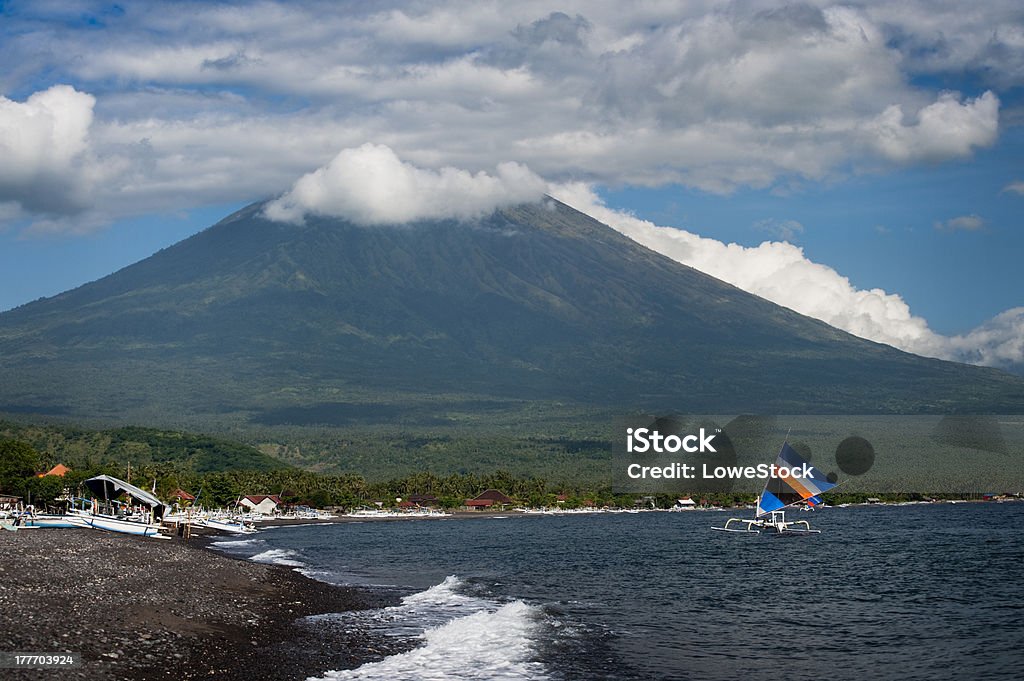 Mt. Agung, Amed, Bali. The active volcano, Mt. Agung, looms over the small fishing village of Amed on the east coast of Bali, Indonesia. Fishermen use colorful sails to power their fishing boats. Asia Stock Photo