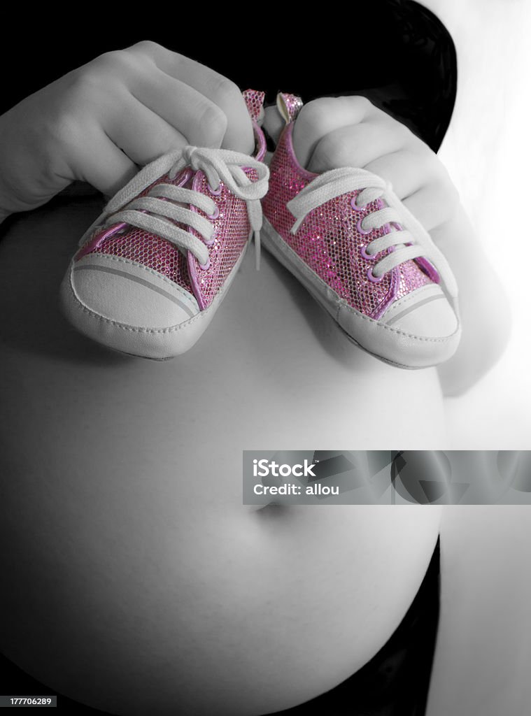 Pregnant girl holds funky pumps up to bump Pink colour-popped image of pregnant girl and her first purchase for baby Adult Stock Photo