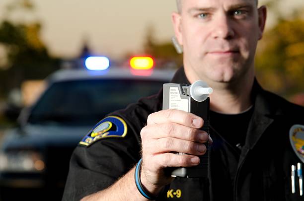 DUI Stop A police officer holds a breath test machine in his hand ready at a traffic stop with his patrol car in the background.*the officer was blurred on purpose to place focus on the mouth piece. emergency services equipment stock pictures, royalty-free photos & images
