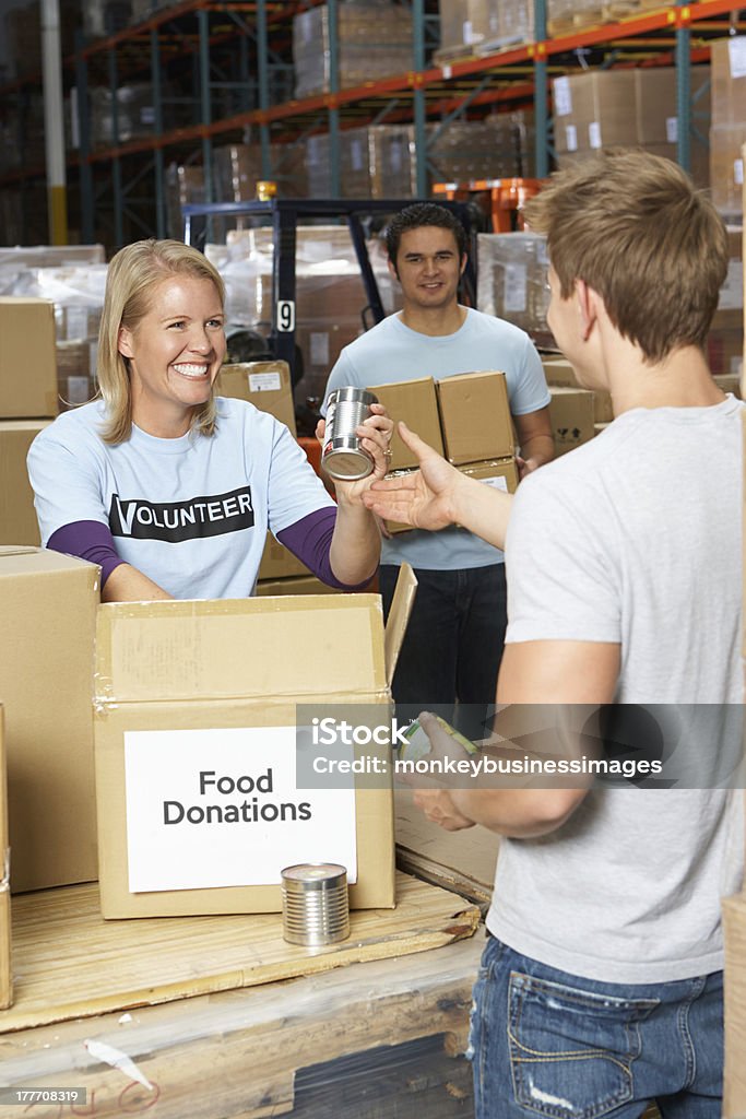 Volunteers Collecting Food Donations In Warehouse Volunteers Collecting Food Donations In Warehouse Holding Food Can Smiling Food Bank Stock Photo