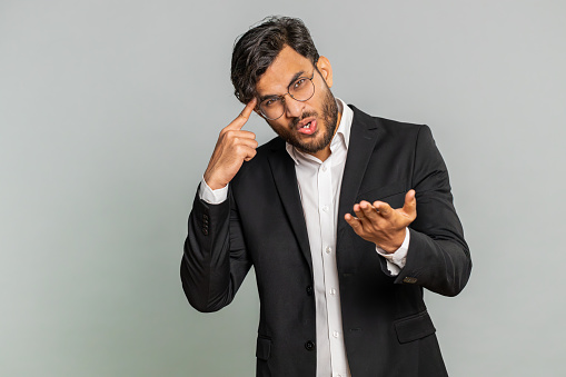 You are crazy, out of mind. Confused Indian businessman pointing at camera and showing stupid gesture, blaming asking some idiot for insane plan, bullying. Arabian man isolated on gray background
