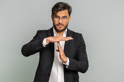 Tired serious upset Indian businessman showing time out gesture, limit or stop sign, no pressure, I need more time, take a break, relax, rest, help. Arabian man guy isolated on gray studio background