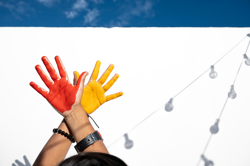 Photoshoot of people doing different expressions with painted hands, balloons, sheets with red and orange colors during a sunny day and indoors scenes