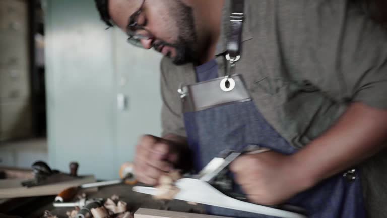 Young man working with a hand planer at a bench in her carpentry shop