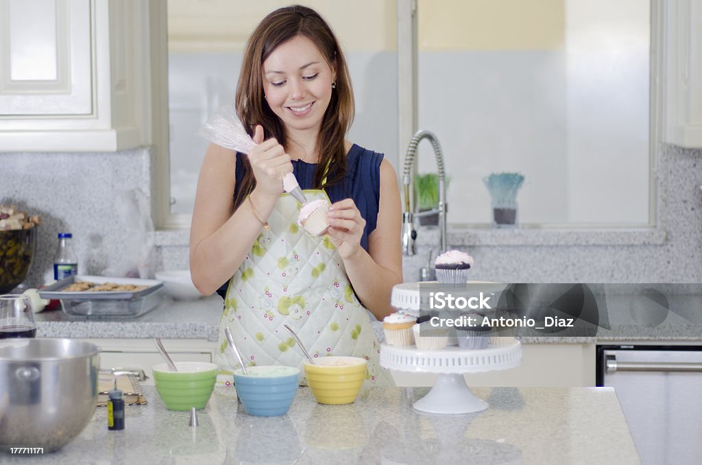 Pretty housewife making cupcakes Cute young brunette decorating cupcakes in the kitchen Adult Stock Photo