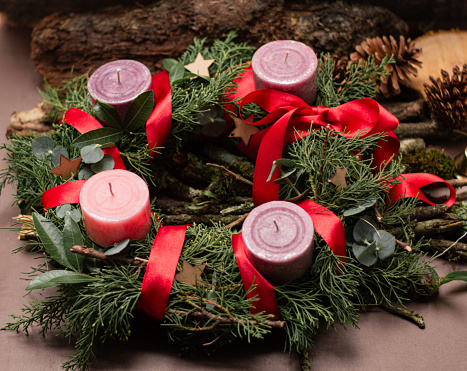 Four red Advent candles are burning. Aside laying pine cone and twig with star anise. On table with red tablecloth. Soft focus on first candle. Useful Christmas background for greeting card.