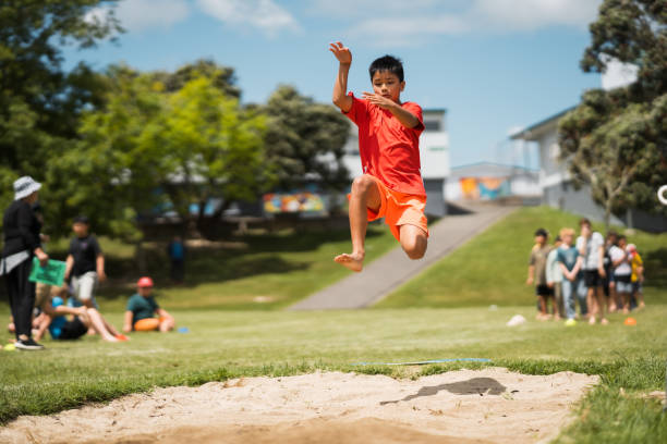 малыш принимает участие в прыжках в длину на школьных соревнованиях. - school sport high up long jump стоковые фото и изображения