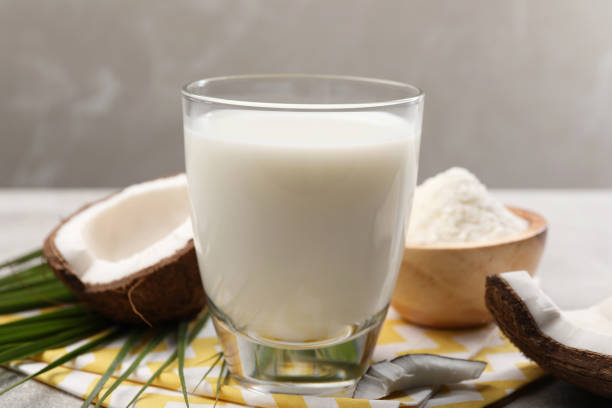 istock Glass of delicious coconut milk, flakes, palm leaf and coconuts on light grey table 1777124828