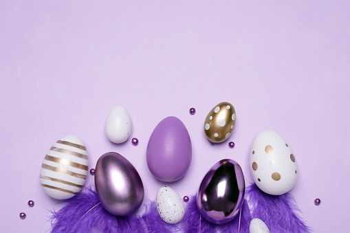 Flat lay composition with festively decorated Easter eggs on lilac background. Space for text