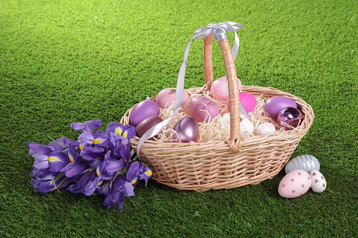 Easter basket with painted eggs and iris flowers on green grass