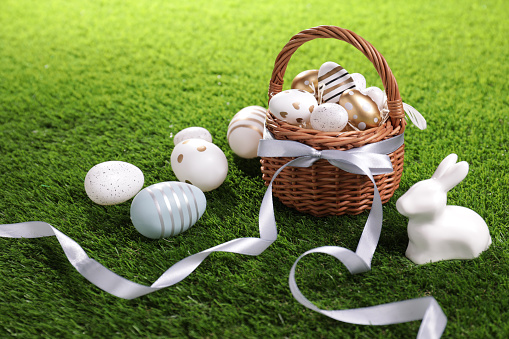 Easter basket with beautifully painted eggs, ribbon and figure of rabbit on green grass