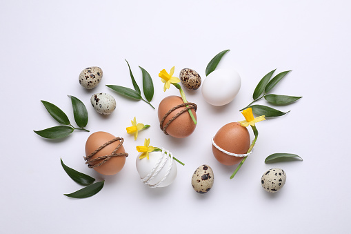 Easter eggs decorated with flowers and green leaves on white background, flat lay