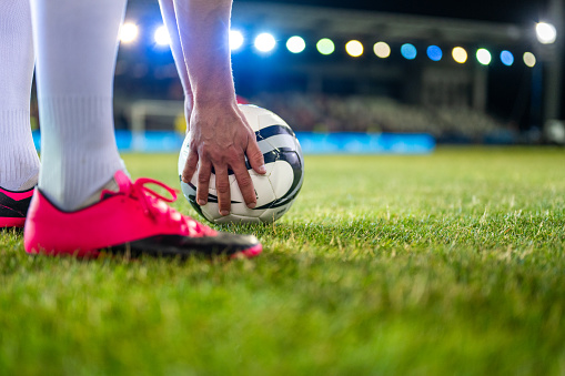 Soccer player putting sports ball on field grass close up