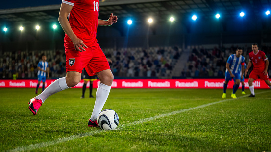 Male soccer player in red uniform doing kick off on sports field, legs cropped medium shot