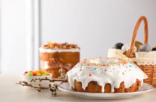 Delicious Easter cake decorated with sprinkles near willow branches on white wooden table. Space for text