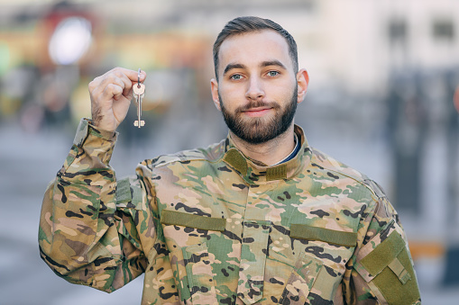 A soldier in camouflage uniforms shows house keys, mortgage assistance from a veterans organization