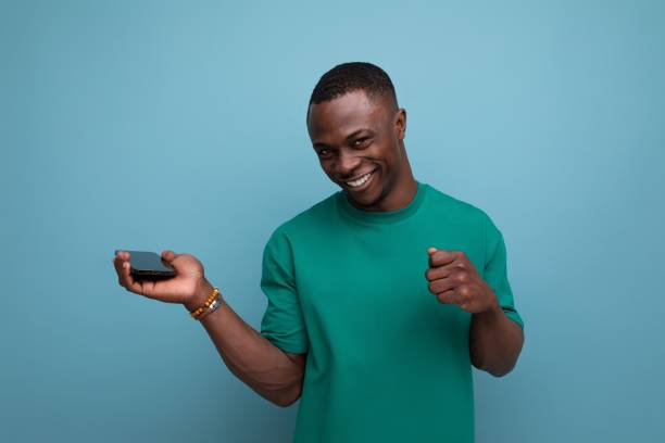 istock young smart african guy with short haircut dressed in a basic t-shirt holds a smartphone in his hand and smiles against the background with copy space 1777163689