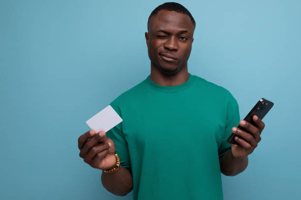 istock a young african guy with a short haircut dressed in a basic t-shirt uses a smartphone for transfers from a bank card on the background with copy space 1777164204