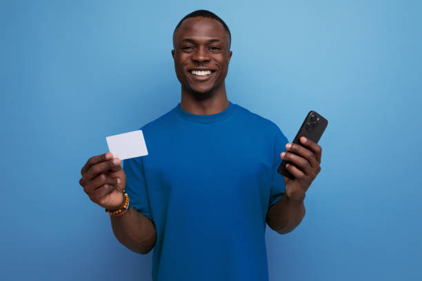 istock 30 year old handsome pleasant with dark skin american man dressed in a basic t-shirt holding a smartphone and a plastic card for shopping on the background with copy space 1777164221