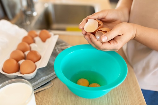 A woman breaks eggs into a deep bowl.