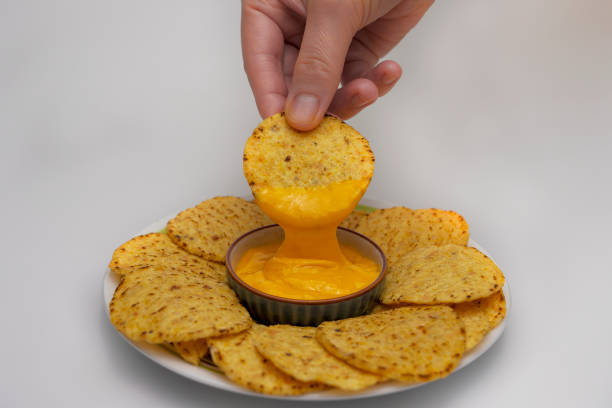 A hand dipping nachos into cheese sauce on a plate