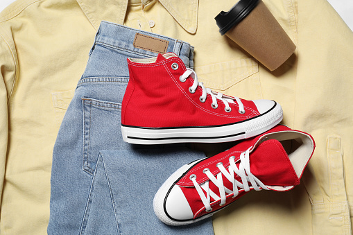 Pair of stylish red shoes, jeans and paper cup on yellow shirt, flat lay